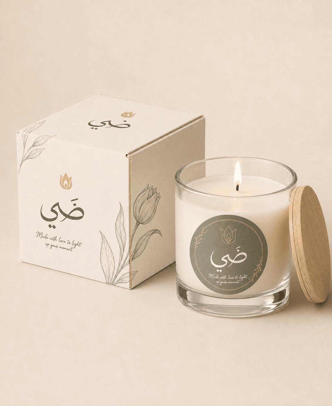 شمعة ضيّ مشتعلة في كوب زجاجي بملصقها الزيتوني، بجانب علبتها الكريمية المزيّنة برسوم نباتية